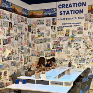 two children sit at a table in front of a creation station